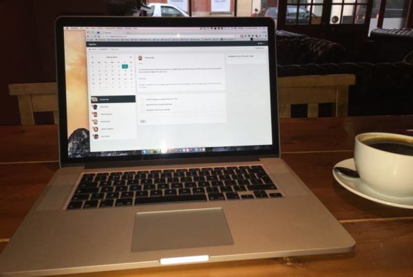 Open laptop pictured next to a cup of coffee in a cafe