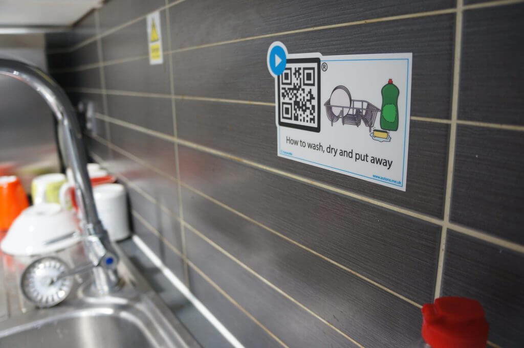 A photo of a stainless steel sink with a QR code taped to the wall above it.